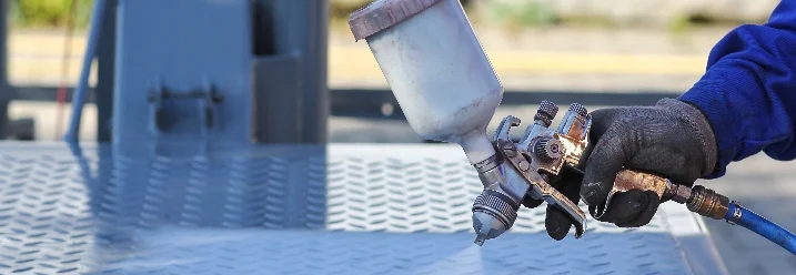 Person lackiert Metallplatte mit Spritzpistole